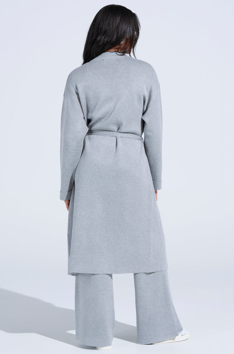 Rear view of a person with long dark hair in a light gray COZY LUXE KNIT TRENCH, featuring an oversized silhouette and matching wide-leg pants, set against a white background.