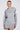 A person with tied-back hair in the BETTER OFF SWEATER JERSEY DRESS, a gray hoodie with white striped sleeves, pleated hem, mini silhouette, drawstring, and front pocket. They're wearing hoop earrings against a plain background.