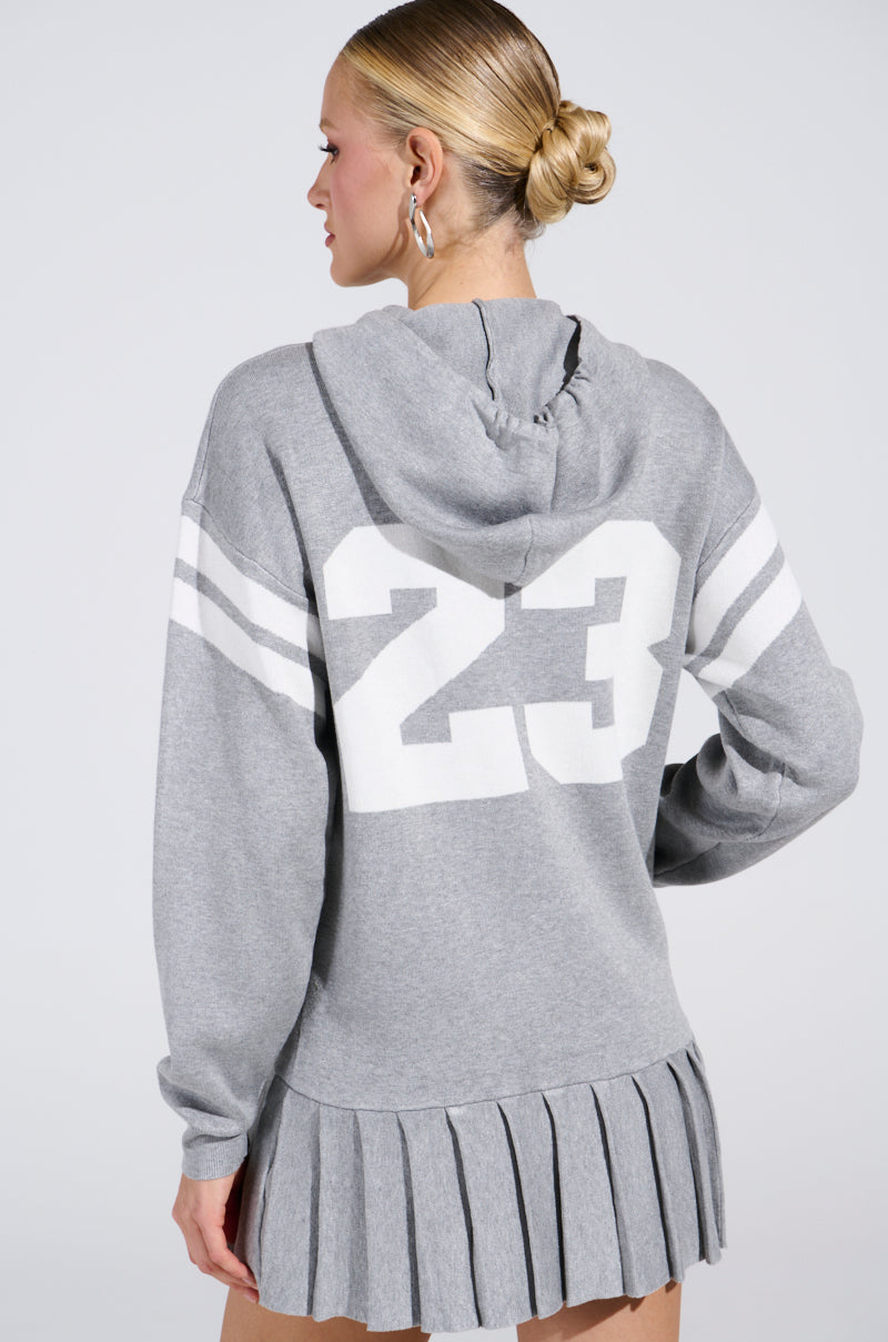 A woman in a BETTER OFF SWEATER JERSEY DRESS with the number 23 on the back stands with her hair pulled back, facing away from the camera.