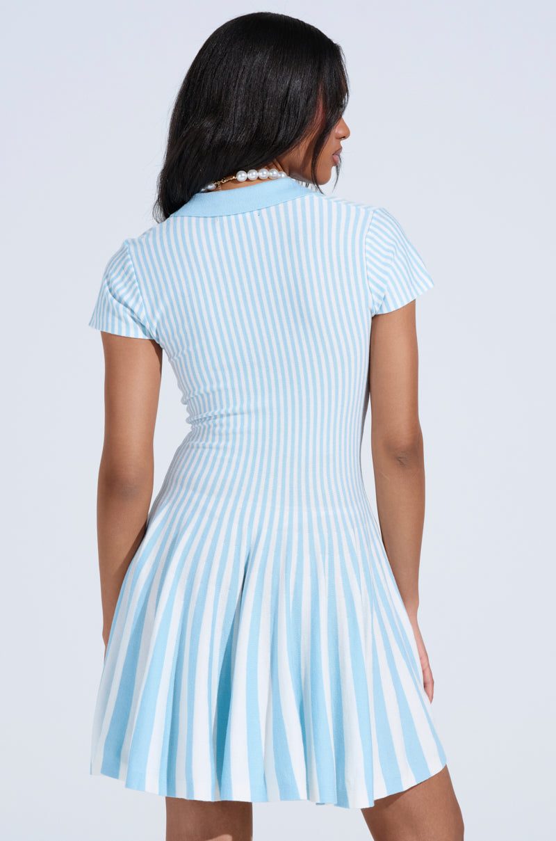 A person with long dark hair is seen from the back wearing the ALINA PLEATED KNIT FIT AND FLARE MINI DRESS IN BLUE, featuring light blue and white vertical stripes, standing against a light background.