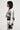 A person with short dark hair is wearing a matching black and white KALEIDOSCOPE DREAM PULL OVER SWEATER and skirt. They are standing in profile against a plain white background, their ensemble boasting an abstract wavy pattern that adds depth to the otherwise minimal setting.