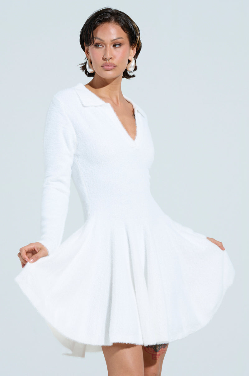 Modeling a white COZY GIRL CHIC FUZZY KNIT MINI DRESS WITH LONG SLEEVES, they pose against a light gray backdrop. The dress features a V-neckline and flared skirt, complemented by wet-look hair and hoop earrings.
