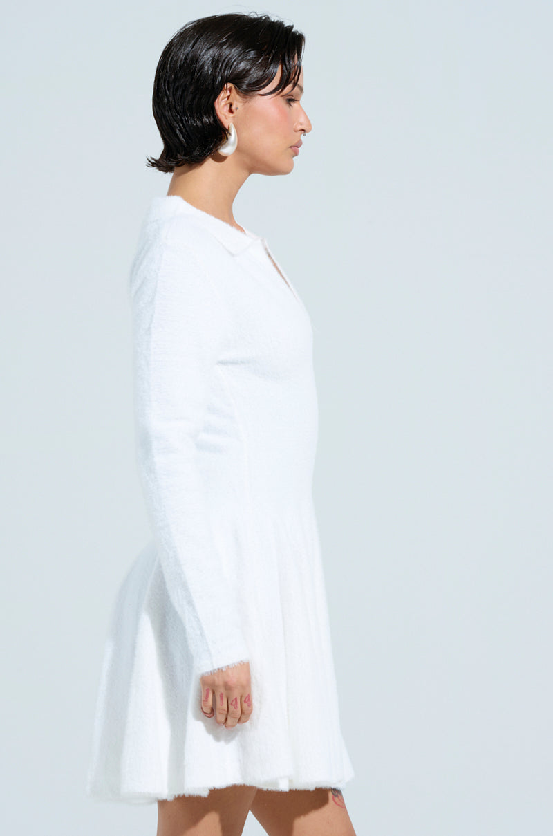 A person with short dark hair models the Cozy Girl Chic Fuzzy Knit Mini Dress with long sleeves against a light gray background, embodying cozy girl chic style. They wear pearl-like earrings and maintain a neutral expression.