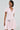 The BOW DOWN GIRL MINI DRESS IN PINK, with a mohair-like knit and small bow details, features a skater silhouette with short sleeves, a V-neck, and a flared skirt. A sparkly chain belt and earrings add flair against the neutral background, exuding confidence.