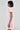 A person with short black hair is in profile wearing the BOW DOWN GIRL MINI DRESS IN PINK adorned with small bows and white hoop earrings, featuring a skater dress silhouette that adds charm against a plain light grey background.