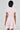 A person with short dark hair is wearing the Bow Down Girl Mini Dress in pink, featuring small bows, short sleeves, and a skater dress silhouette. They stand with their back to the camera against a plain light background.