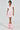 Wearing a BOW DOWN GIRL MINI DRESS IN PINK, a person stands confidently in short sleeves with a skater silhouette. Fluffy pink boots and a mohair-like short hairstyle complete the look against a plain white background.