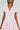 A woman elegantly showcases the Bow Down Girl Mini Dress in pastel pink, featuring a fuzzy mohair-like knit, short sleeves, a skater dress silhouette with a deep V-neck and collar, and small bow details. She complements it with pearl earrings and straight-styled hair.