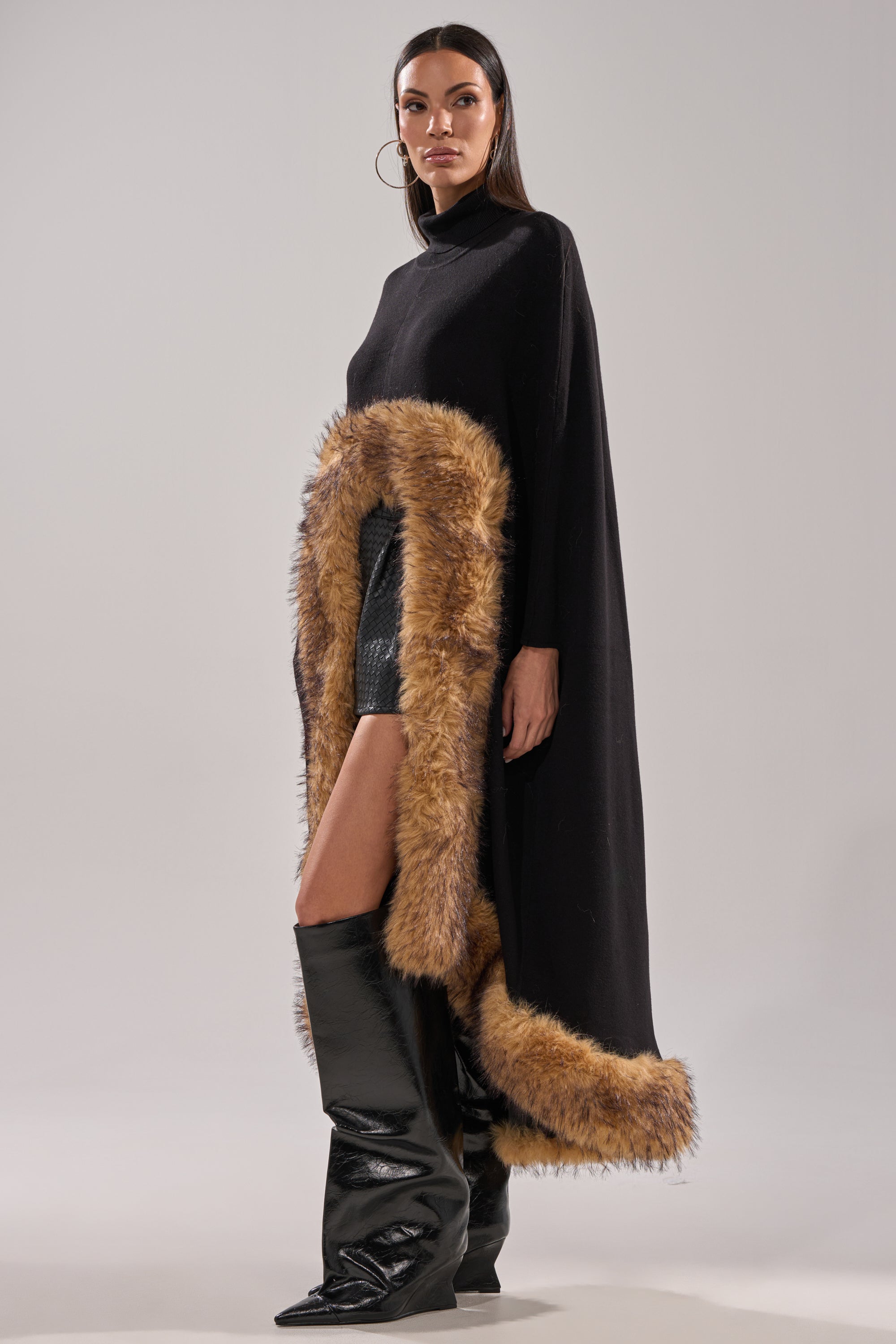A woman wearing the RICH SWEATER WITH FUR TRIM, styled with a black mini skirt and knee-high boots, poses confidently against a light background—a chic winter layering piece. 5