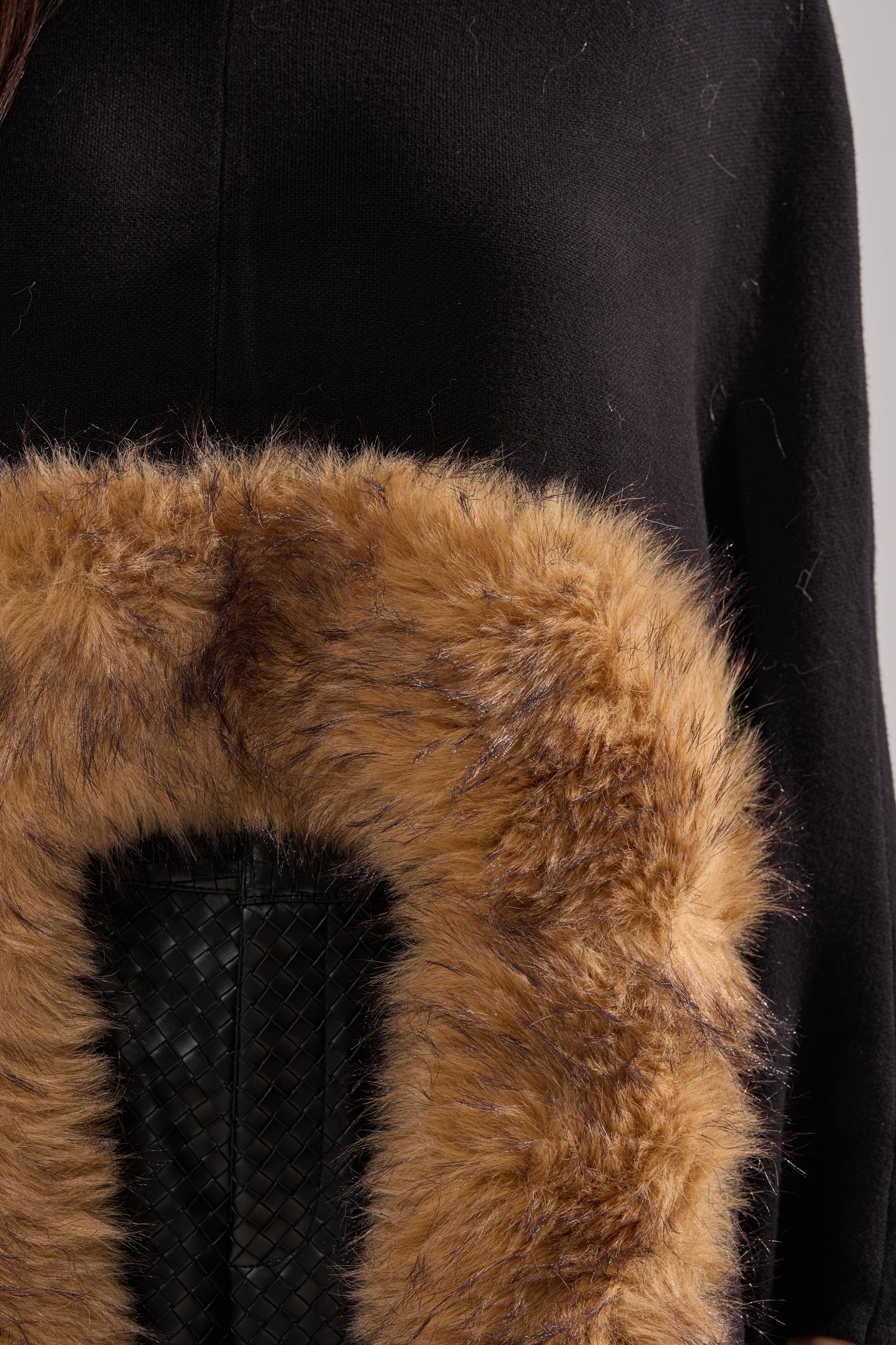 Close-up of a person wearing the RICH SWEATER WITH FUR TRIM, featuring a large, fluffy brown fur trim and black textured woven leather detail underneath. Fur and garment fibers are visible. 7