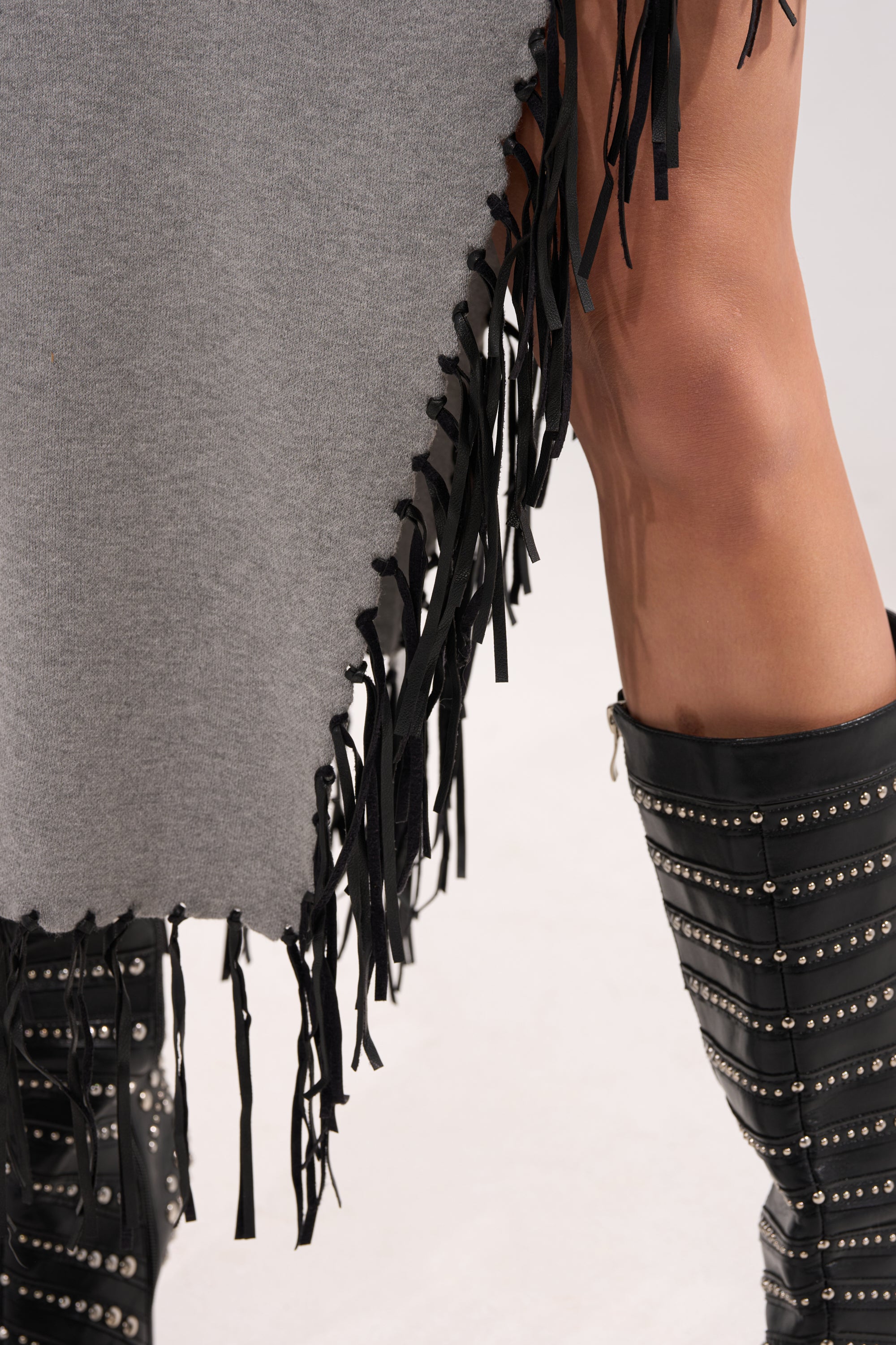 A close-up of a person wearing the SWEATER WEATHER KNIT MIDI DRESS IN GREY, styled with knee-high black boots featuring silver studs and horizontal straps.