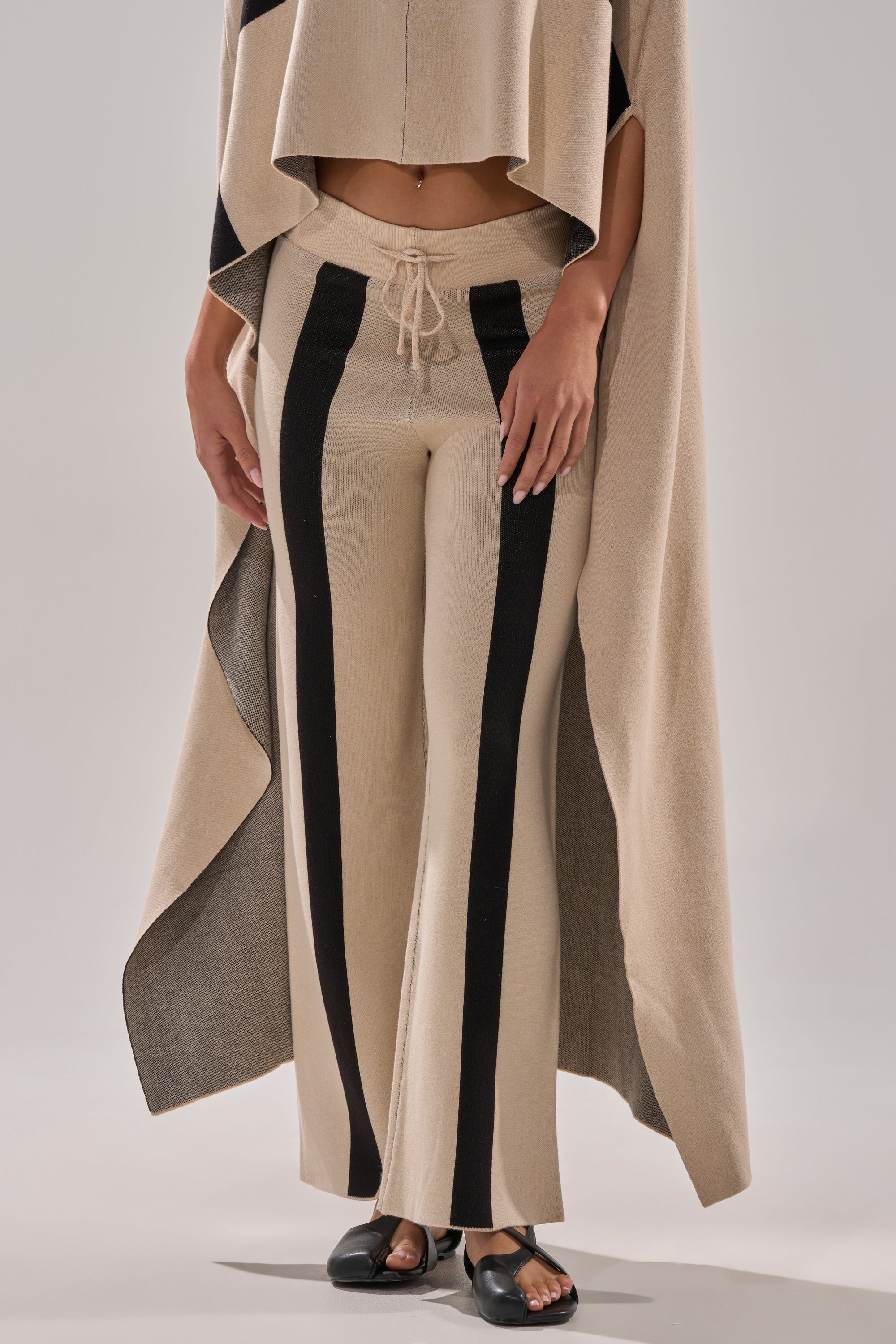 Model wears the CLAUDIA SWEATER WIDE LEG PANT with beige and black stripes, paired with a matching poncho top and black sandals. Photo is cropped at the shoulders.