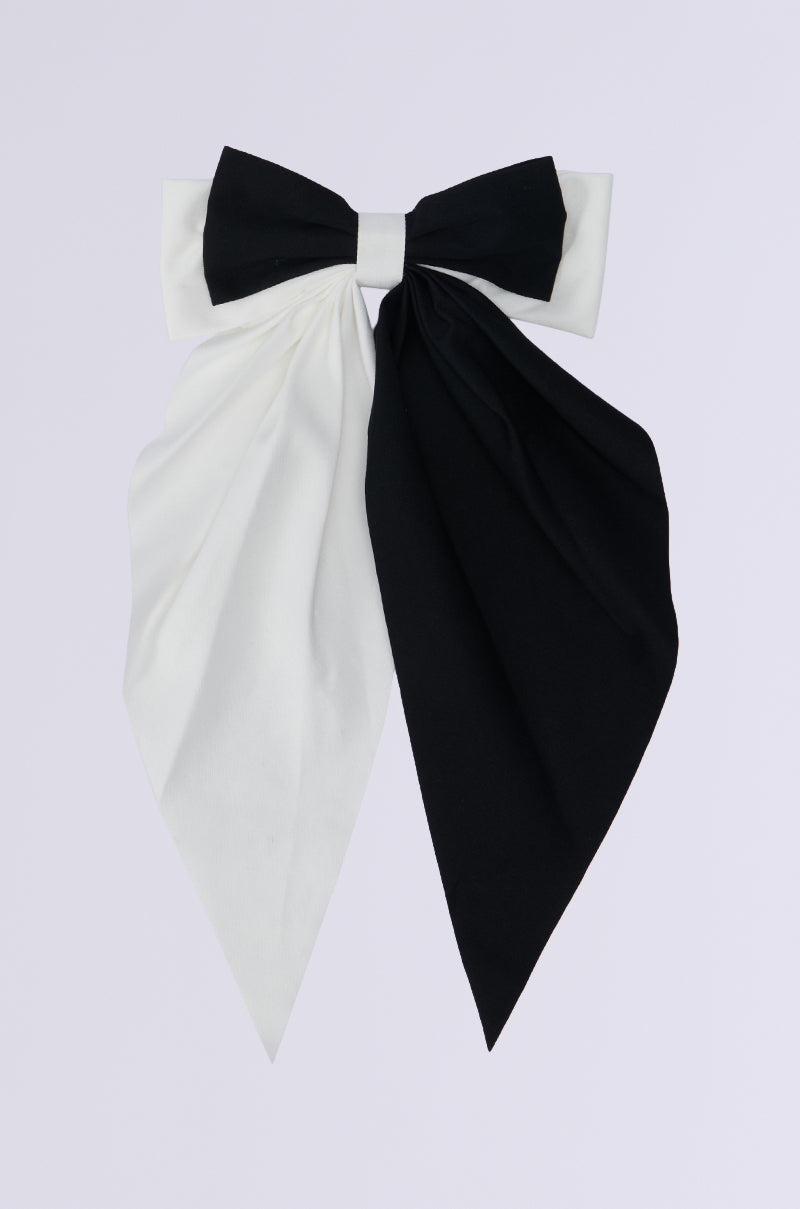 The SPLIT DECISION HAIR BOW showcases an oversized design with a large silhouette and two long tails featuring a striking colorblock pattern: black on the right and white on the left, set against a plain background. 2
