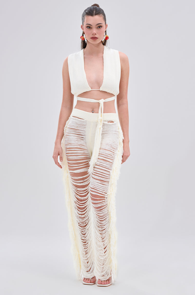 A woman models the BEST DRESSED FRINGE BRALETTE AND LEGGING set, featuring a white fringe bralette and high-waisted sheer leggings with long horizontal slits and a stretchy elastic waistband. She has long dark hair tied back and red earrings.