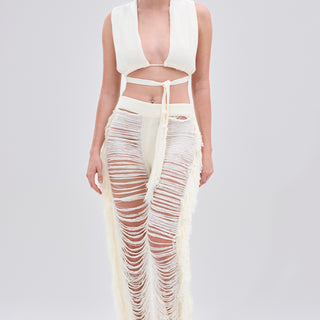 A woman models the BEST DRESSED FRINGE BRALETTE AND LEGGING set, featuring a white fringe bralette and high-waisted sheer leggings with long horizontal slits and a stretchy elastic waistband. She has long dark hair tied back and red earrings.