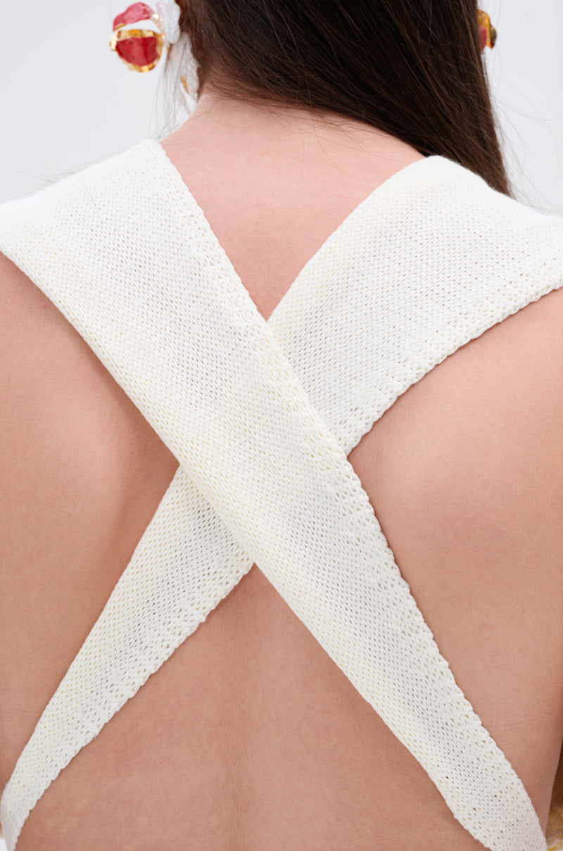Close-up of a person wearing the BEST DRESSED FRINGE BRALETTE with wide X-shaped white knit straps, paired with matching leggings featuring a stretchy elastic waistband. Long dark hair and a red stone earring complete the look.