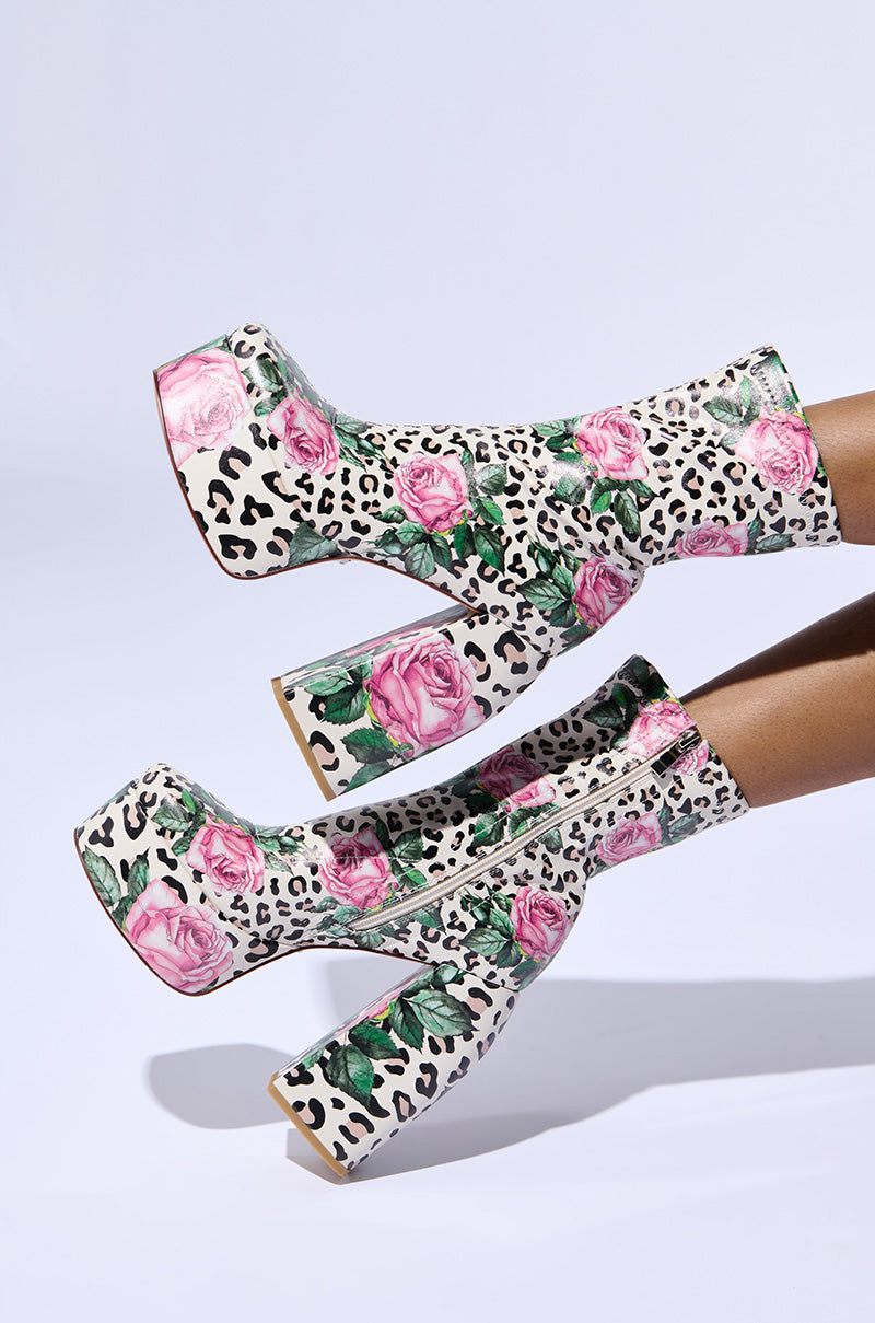 The AZALEA WANG HADLEIGH LEOPARD AND FLORAL PLATFORM BOOTIE features a vibrant and daring design, combining pink and green rose patterns with black and white leopard spots. These booties, set on a chunky high heel, create a striking visual contrast against a plain white background.