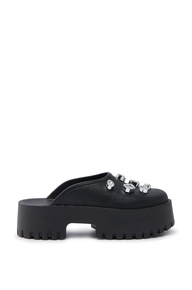 AZALEA WANG HAIN BLACK EMBELLISHED FLAT features a chunky platform sole, ridged tread, and three silver decorative buckles on the faux leather upper. Photographed from the side against a white background.