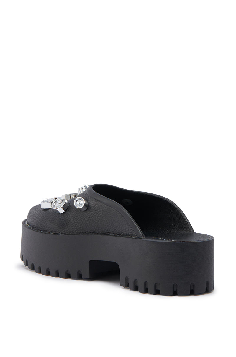 The AZALEA WANG HAIN BLACK EMBELLISHED FLAT is a chunky black platform slide sandal in faux leather, featuring a thick ridged sole and decorative silver embellishments on the upper, shown from the back.