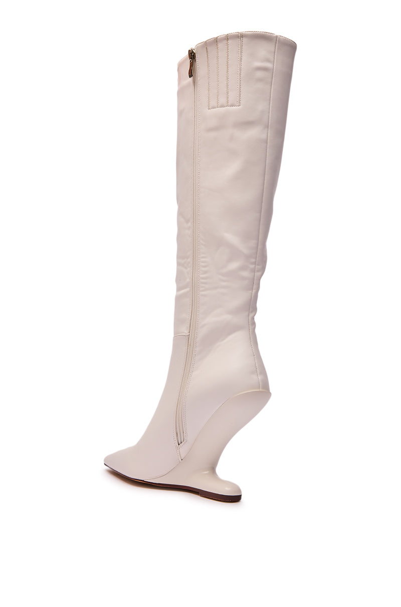 The AZALEA WANG HAKIM WHITE WEDGE BOOT is a knee-high, white faux leather boot with a side zipper and unique curved wedge heel, displayed from a side view on a white background.