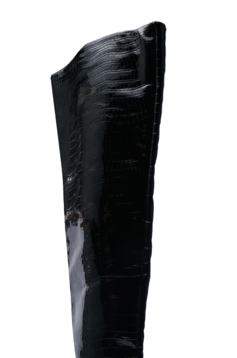 The AZALEA WANG HALINA BLACK CROC STILETTO BOOT features a close-up view highlighting its tall, glossy finish and pointed toe silhouette. Crafted from faux crocodile leather, the boot showcases elegant curves and a shiny texture that stands out against the plain white background, emphasizing its sleek and sophisticated design.