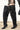 A person wearing the AZALEA WANG HALINA BLACK SNAKE THIGH HIGH BOOT and a mini skirt stands on a sidewalk. Only their legs in the textured, oversized stiletto boots and part of the outfit are visible.