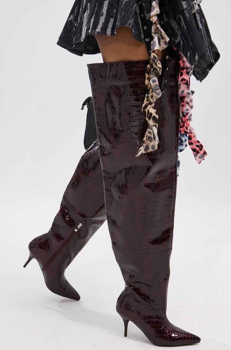 Wearing the AZALEA WANG HALINA BURGUNDY CROC STILETTO BOOT with a thigh-high faux crocodile shaft, this look pairs the shiny boots with a black and white skirt featuring colorful, patterned fabric strips.