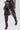 A person wearing the AZALEA WANG HALINA BURGUNDY CROC STILETTO BOOT and a black skirt with colorful animal print accents stands against a plain white background.