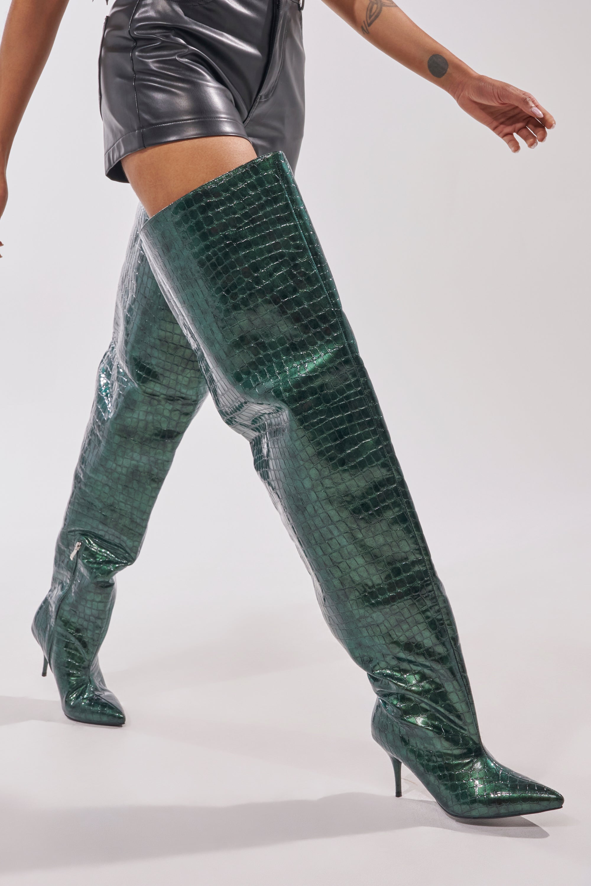 A person in high-waisted black leather shorts and the AZALEA WANG HALINA DARK GREEN CROC STILETTO BOOT poses confidently against a plain light background.