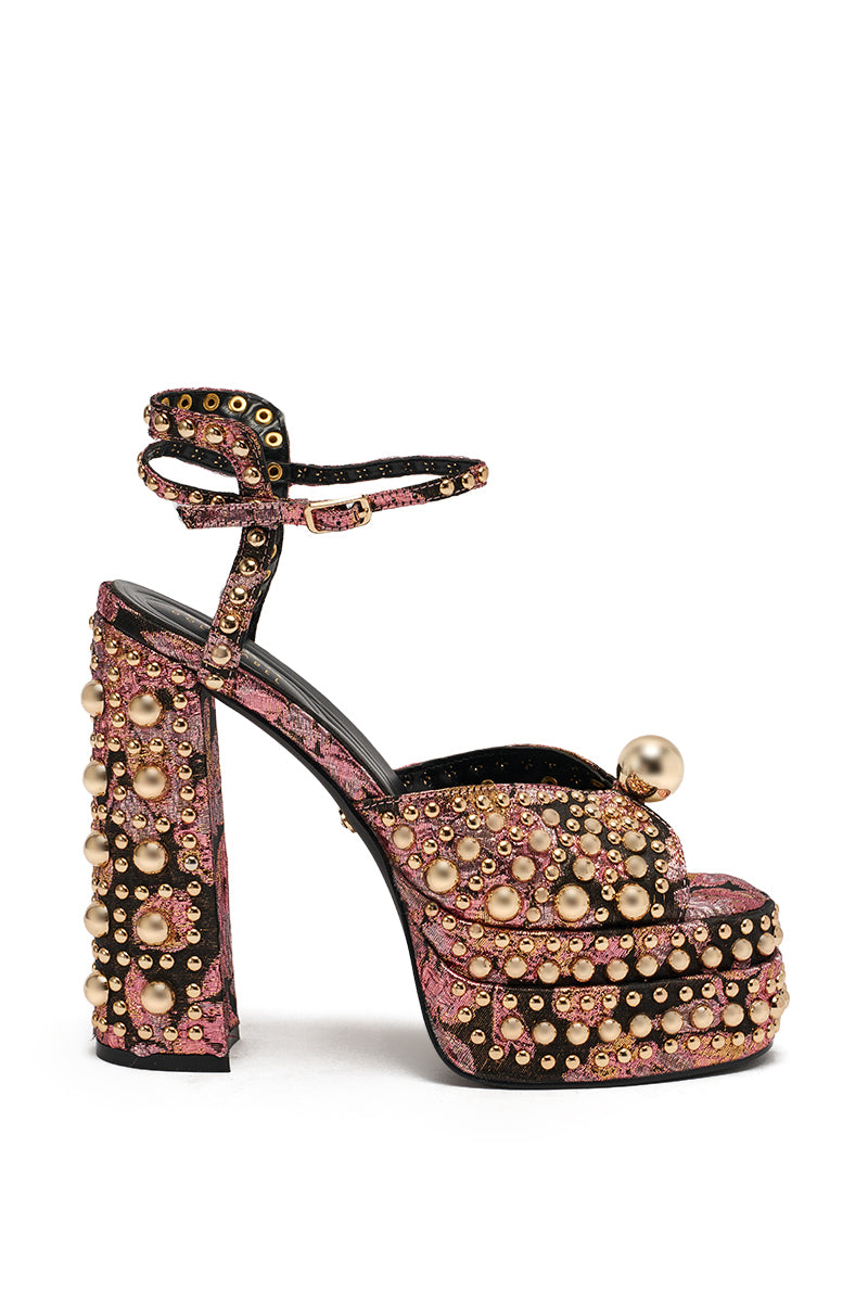 The AKIRA HANNESS BLACK MULTI BROCADE EMBELLISHED CHUNKY SANDAL features a high heel, metallic brocade fabric in pink and black, gold bead and pearl embellishments, an ankle strap, and a chunky platform sole.