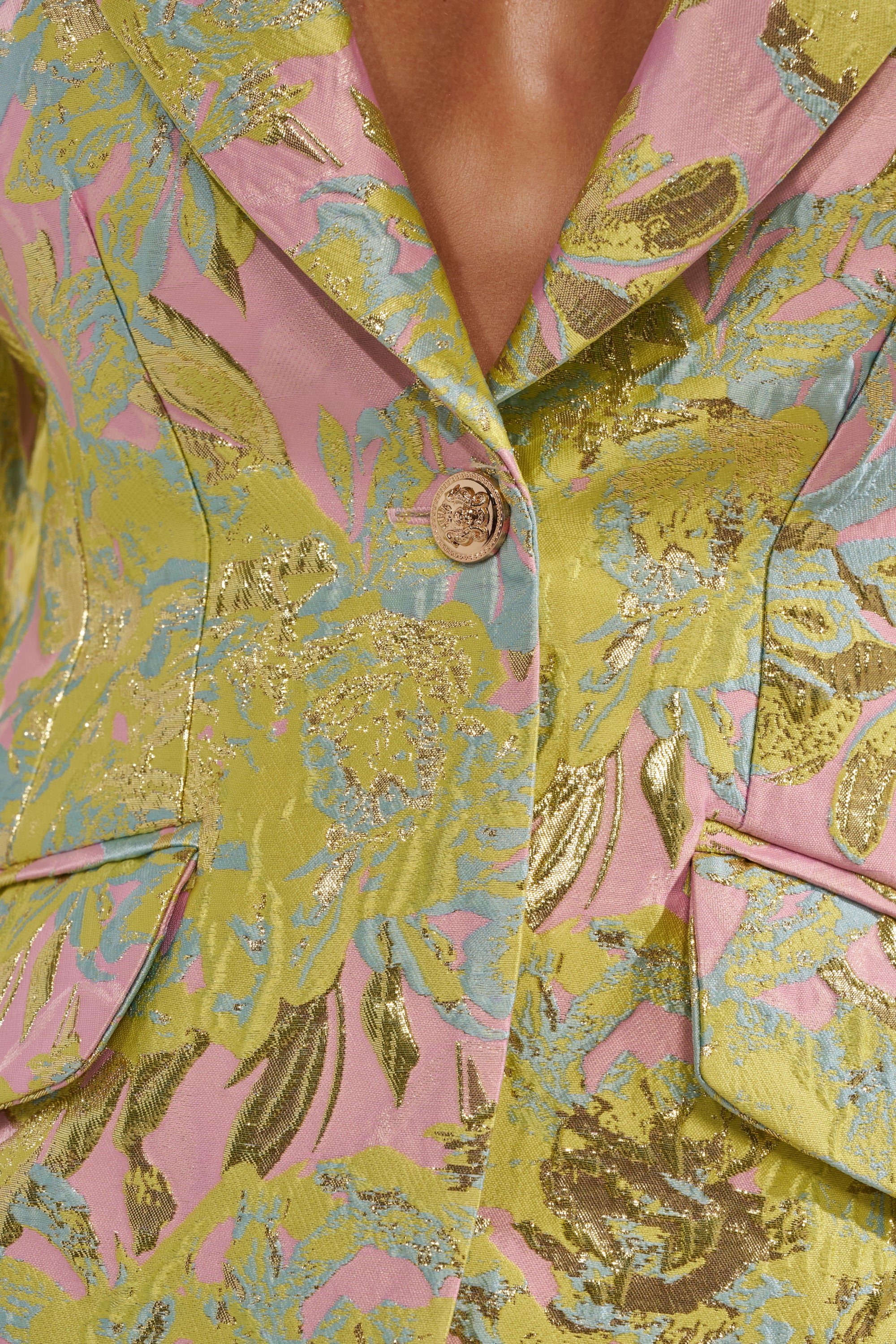 Close-up of the LUCY BROCADE BLAZER, showcasing its metallic fabric with a vibrant yellow, pink, blue, and gold floral pattern, single button closure, and two flap pockets. 9