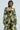 A person wearing the BUY MYSELF FLOWERS BROCADE BLAZER paired with matching wide-legged pants, both featuring a chic black and green floral pattern, poses against a light background. They have short, dark hair and complement their look with metallic hoop earrings.