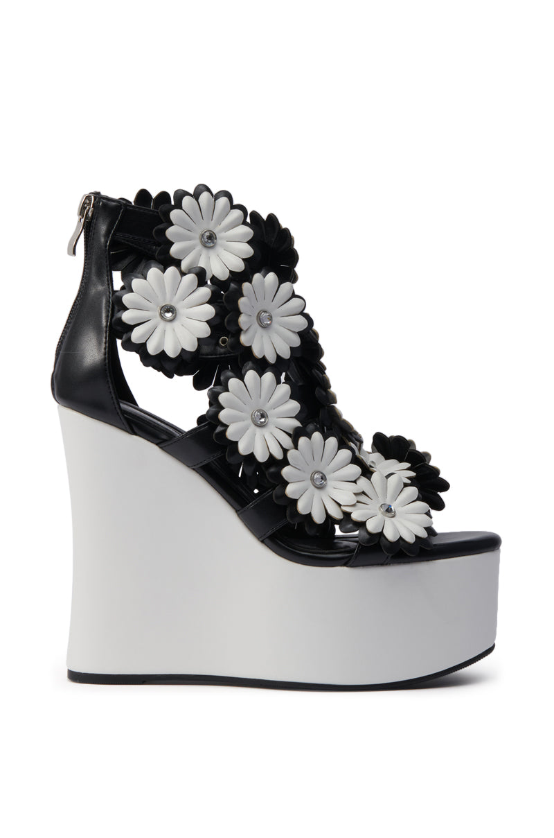 The AZALEA WANG FLOWER EMBELLISHED WEDGE SANDAL IN BLACK features large black and white floral appliques, a back zipper, and a chic wedge heel for a playful yet sophisticated look.