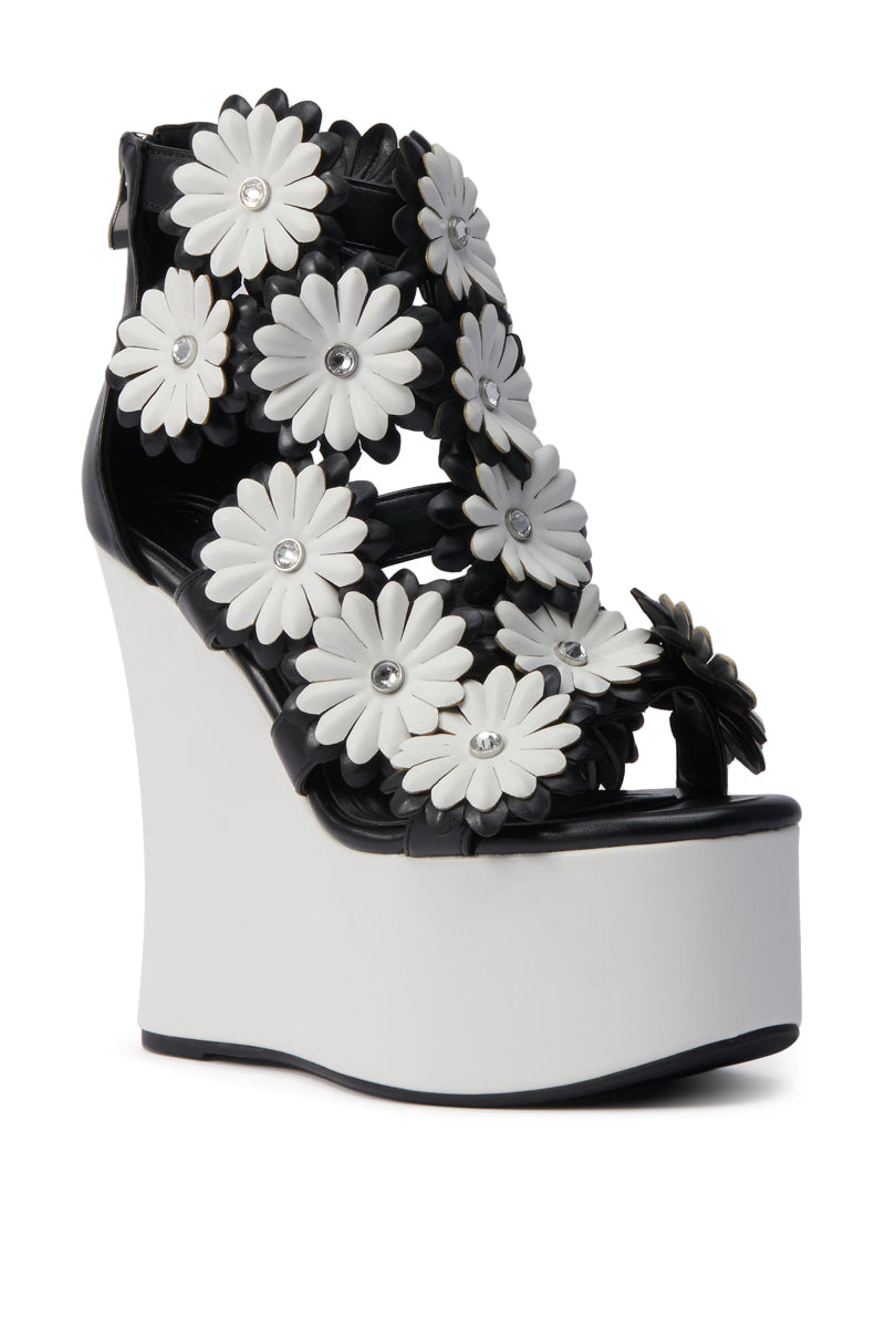 The AZALEA WANG FLOWER EMBELLISHED WEDGE SANDAL IN BLACK features black and white daisy appliques with jeweled centers, multiple daisy-accented straps, and a thick white wedge heel for a chic, playful look.