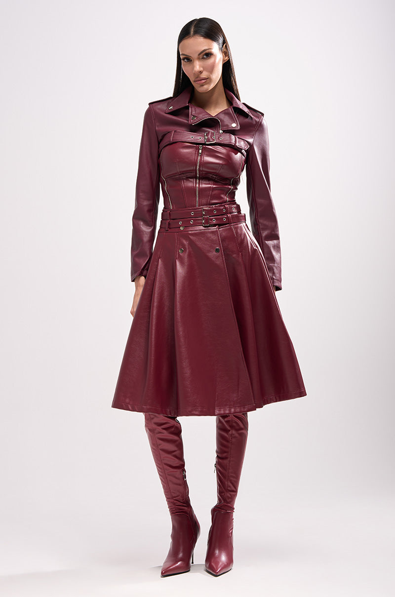 A woman faces forward in the HARLEY LUXE ULTRA CROP MOTO IN BURGUNDY, paired with a matching flared skirt and over-the-knee boots for a chic fall look, set against a plain light gray background.