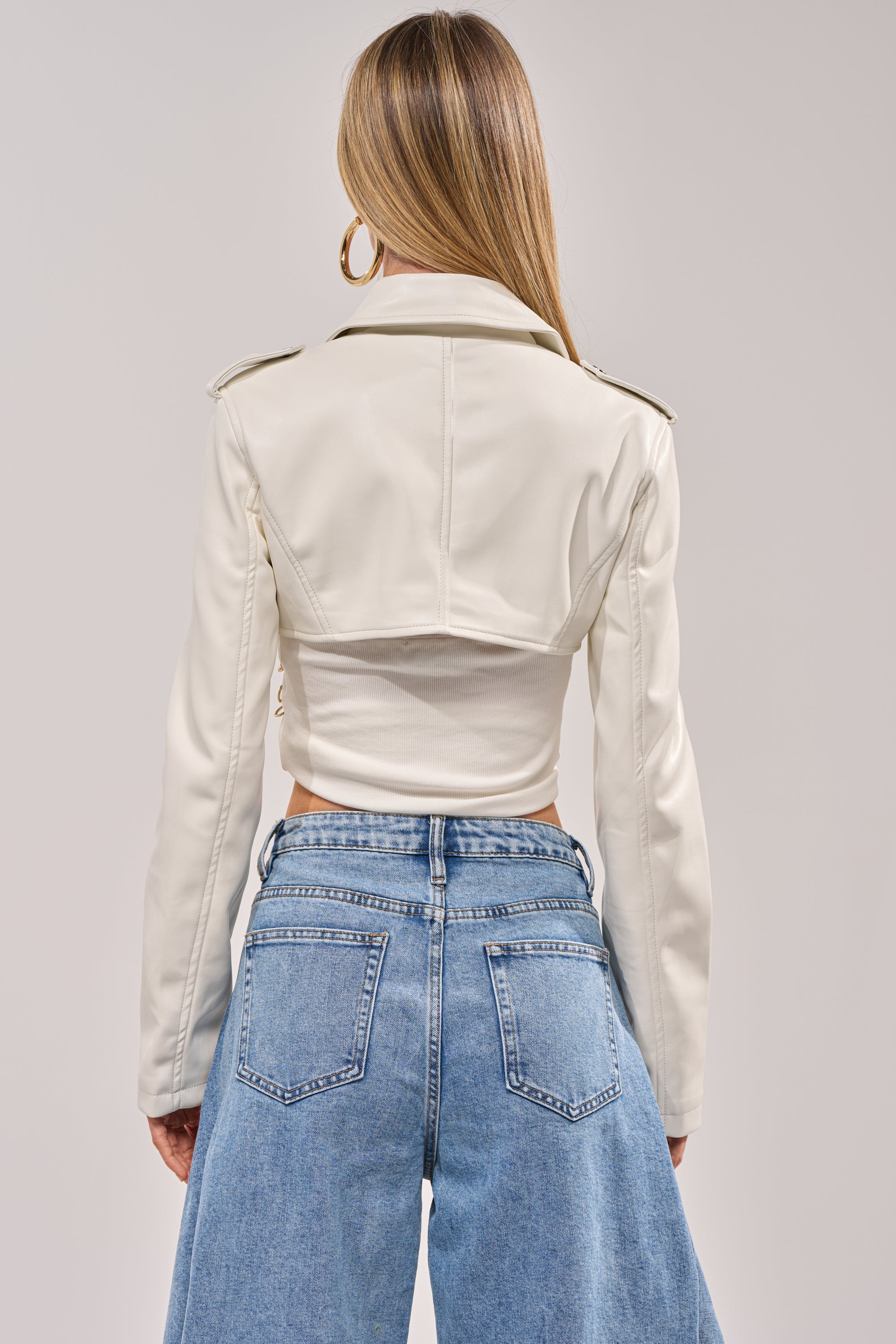 A woman with long, straight hair stands against a plain light background, wearing the HARLEY LUXE ULTRA CROP MOTO IN WHITE and high-waisted blue wide-leg jeans. 5
