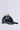 The TOASTIE FAUX FUR POM HAT, featuring a black leather design with a fluffy faux fur pom on top and an adjustable strap, is displayed against a plain light gray background.
