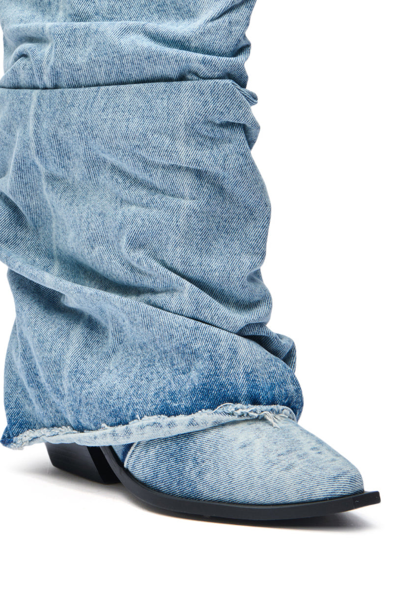 A close-up of a person wearing the AZALEA WANG HAWSTON DENIM WESTERN FOLD-OVER BOOT, featuring light blue denim, a pointed toe, and a flat black sole, styled to look like jeans. 7