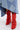 A person in a patchwork denim skirt stands on a light surface, wearing AZALEA WANG HAWKSTON RED RUCHED WESTERN BOOTIE with a chunky heel and slouchy faux suede uppers, partially covered by the skirt.