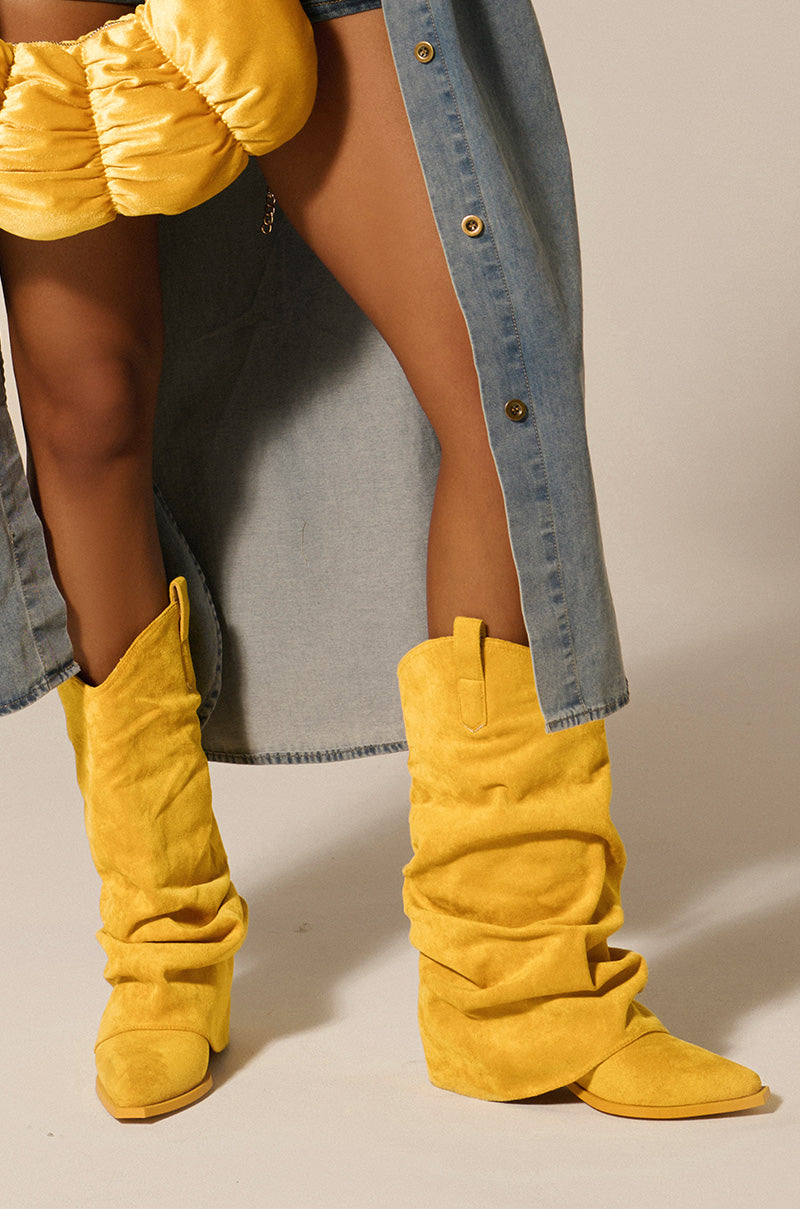 Sporting the AZALEA WANG HAWKSTON YELLOW BOOTIE, a person holds a matching yellow bag, partly concealed by a blue denim skirt.