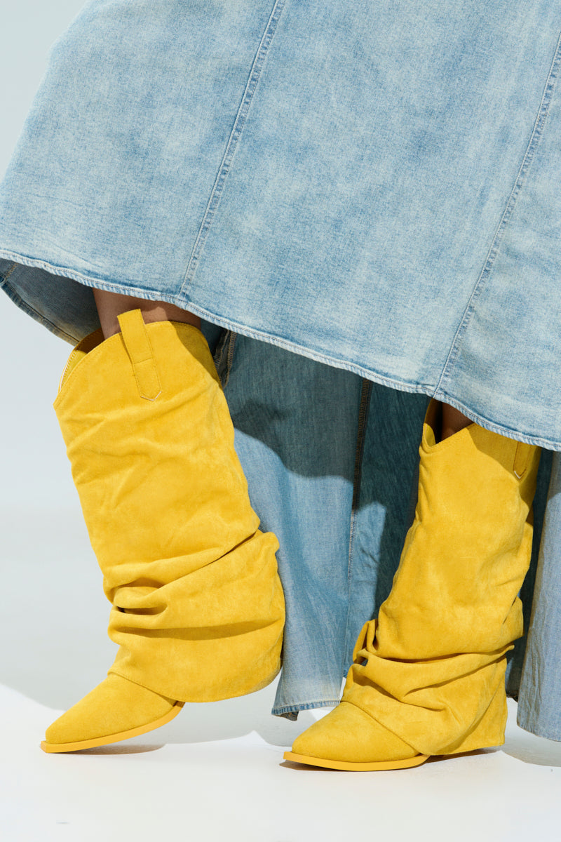Pairing a long, faded blue denim skirt with AZALEA WANG HAWKSTON YELLOW BOOTIES adds a pop of color to the outfit. These bright yellow faux suede booties feature pointed toes and flat soles, set against a neutral, light-colored background.
