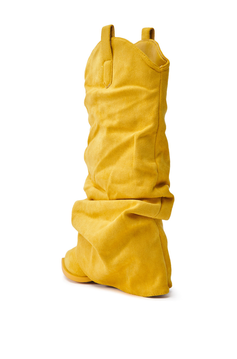 The AZALEA WANG HAWKSTON YELLOW BOOTIE is a slouchy yellow suede bootie with folded fabric and top loops, a slightly pointed toe, and a flat sole, showcased at an angle against a white background.