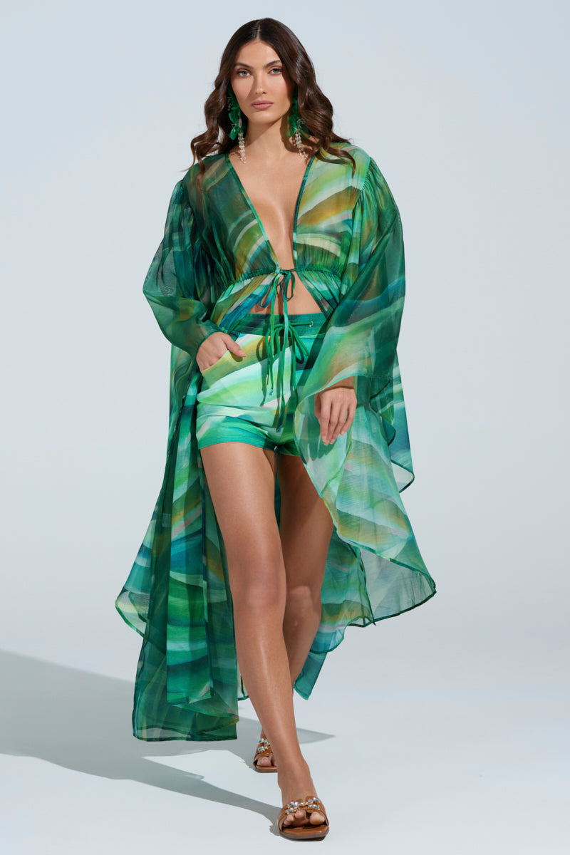 A woman confidently walks in the ON FIRE SET outfit featuring a robe-style top over a matching wavy print crop top and shorts. She pairs it with green earrings, sandals, and her hair is styled in loose waves. 6