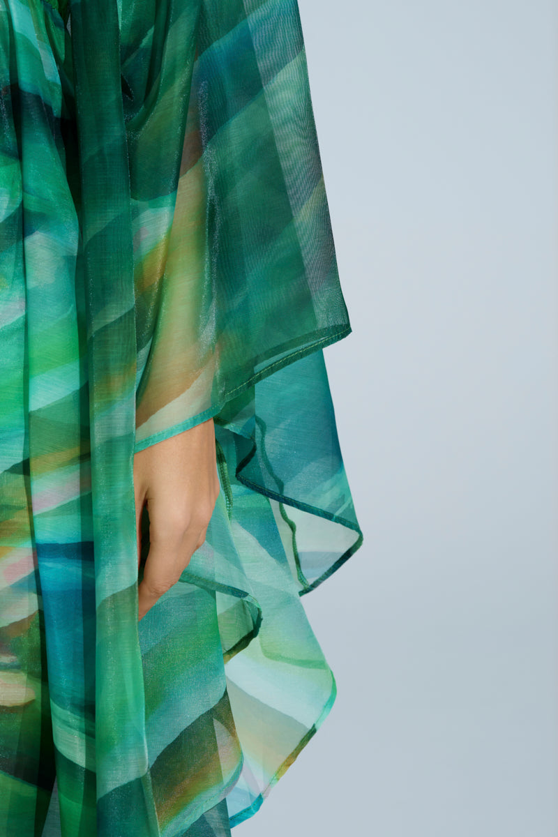 Wearing the ON FIRE SET, a person showcases a robe-inspired top with an abstract green and blue wavy print. A hand emerges near geometric layers against a soft light blue backdrop. 7