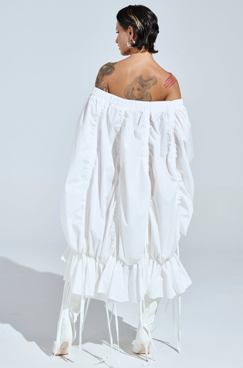 A person with short dark hair poses with their back to the camera, highlighting tattoos on their back and arm while wearing the FREE AS CAN BE MINI DRESS IN WHITE, paired with striking white high-heeled boots against a plain white backdrop.