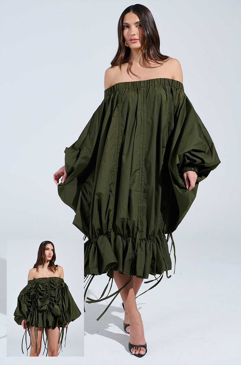 A woman showcases the voluminous "Free as Can Be Mini Dress in Olive," an off-shoulder, oversized piece with ruching and a ruffled hem. She pairs it with black high heels. An inset reveals the dress's intricate texture and features.