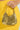 A hand holds the TAYTAY METAL PURSE, a small gold metallic bag with a chain link strap. It contrasts against a textured yellow outfit, set against a simple light background.