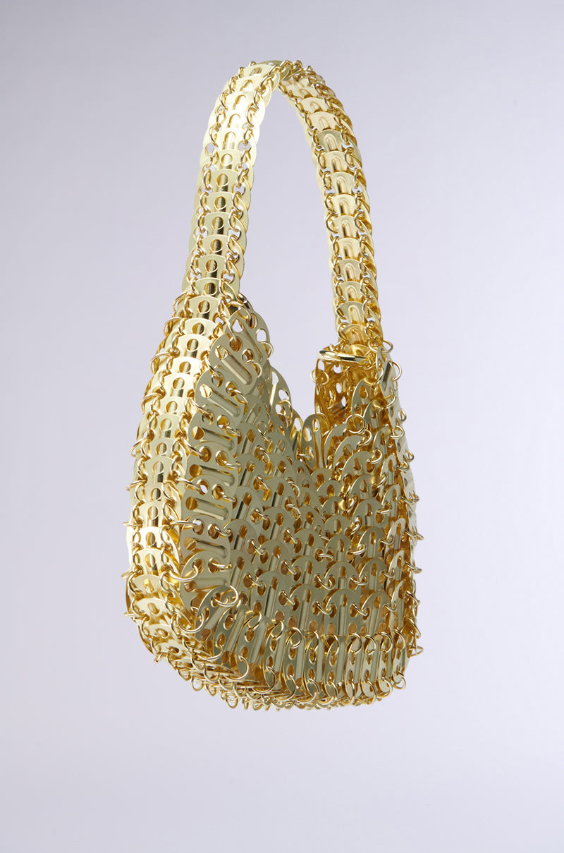 The TAYTAY METAL PURSE is a slouchy mini baguette bag crafted entirely from interlocking gold-colored metal pull tabs, featuring a single chain link shoulder strap, set against a plain gray background. 8