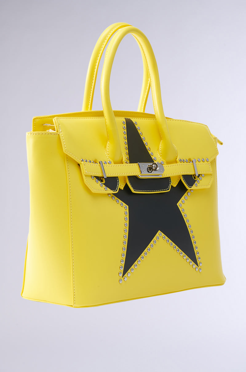 Show off your style with the STAR POWER TOTE—a vibrant yellow faux leather bag featuring a structured shape, bold black star with silver stud accents, dual handles, and a front flap secured by a metal clasp.
