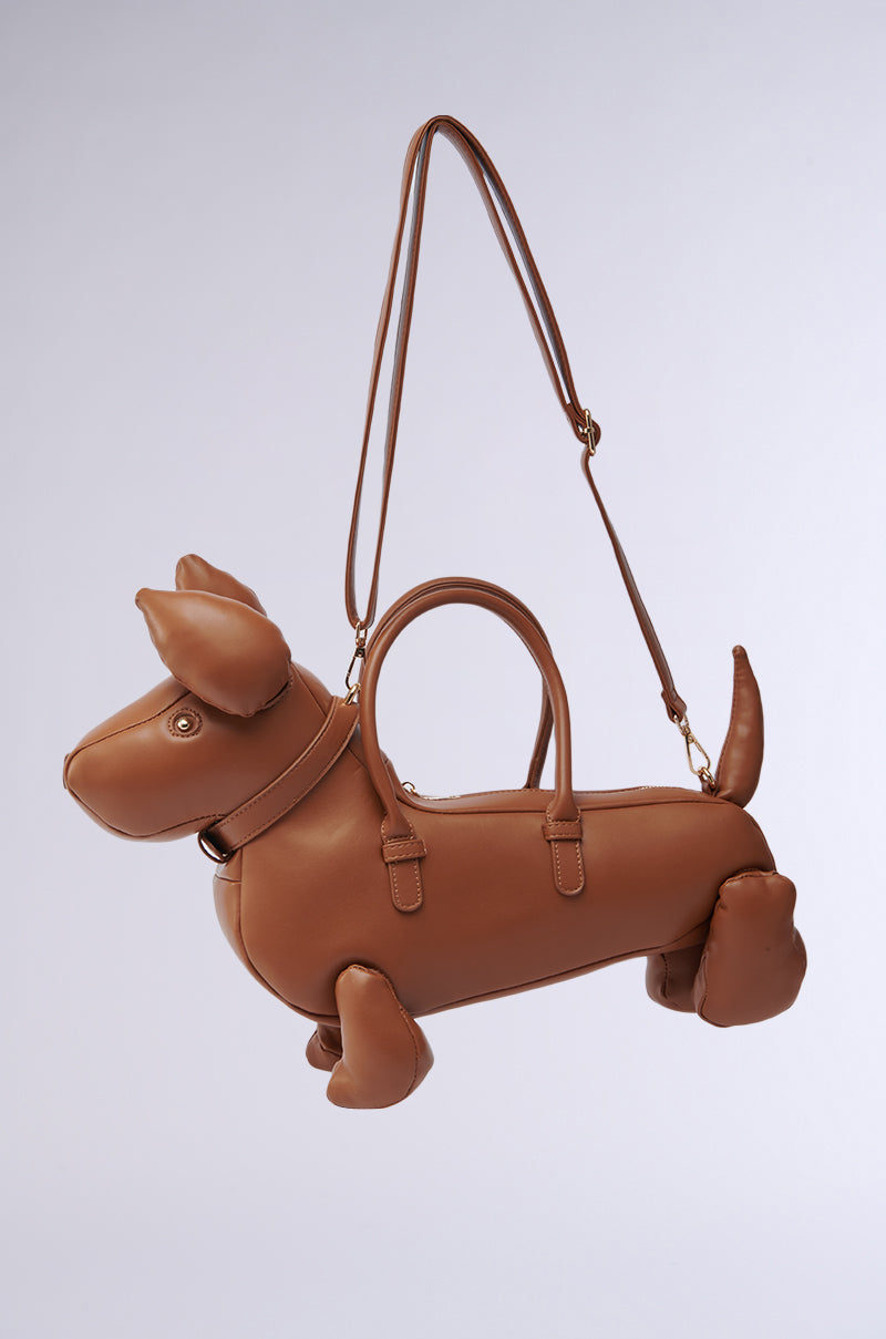 The I'M REALLY A DOG PURSE, a brown novelty bag shaped like a dachshund with ears, legs, tail, and collar, hangs by its shoulder strap against a plain light background.